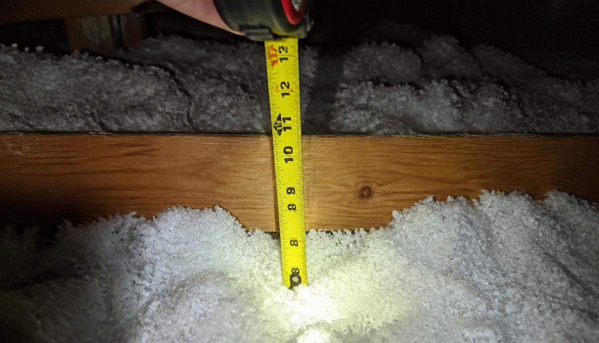 Tape measure checking blown-in attic insulation depth against a ceiling joist in a Denair home.