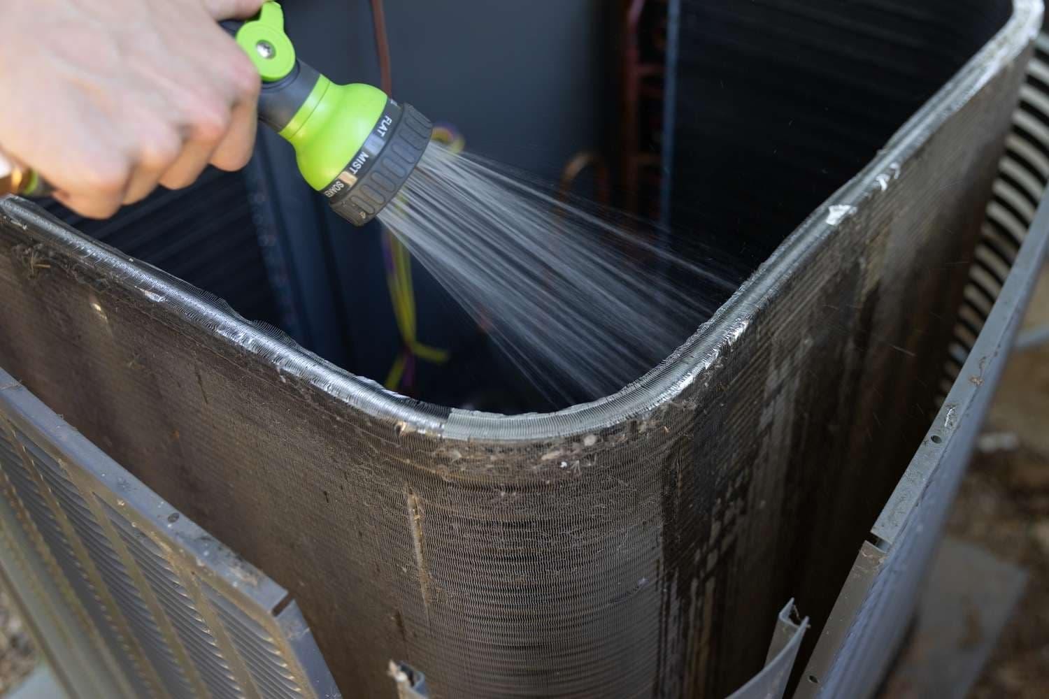 Technician cleaning an HVAC condenser coil with a water spray to remove dirt and debris.