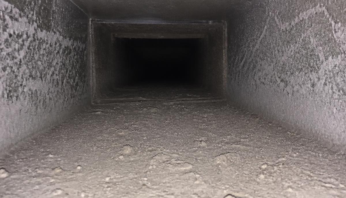Inside of a residential air duct coated in gray drywall dust and construction debris in a new Ceres home